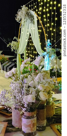 Rustic floral arrangement in jars. Festive decoration, white roses and plant branches in decorative jars. 128552318