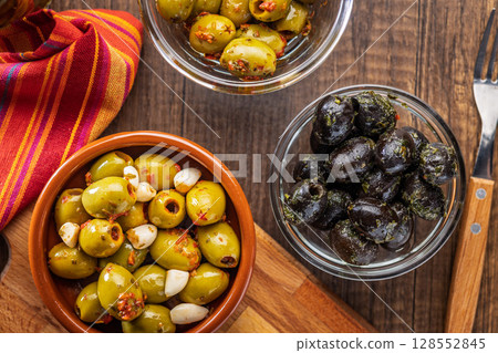Tapas. Flavored pickled olives in bowl on wooden table. Top view. 128552845