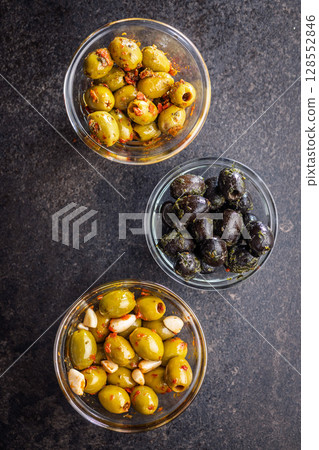 Tapas. Flavored pickled olives in bowl on black table. Top view. 128552846
