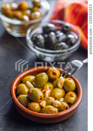 Tapas. Flavored pickled olives in bowl on black table. 128552853