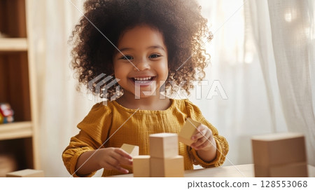 Joyful toddler girl explores tactile play with wooden blocks in a serene, softly lit interior designed for mindful early learning. 128553068