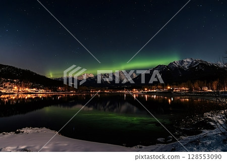 Northern lights illuminating snowy mountain and reflecting in calm lake at night 128553090