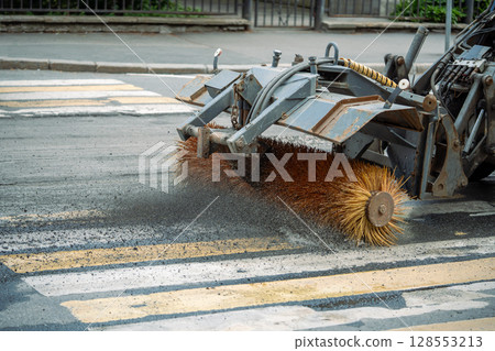 Tractor sweeps gravel from road after repair work at pedestrian cross. City renovation, maintenance Tractor sweeps gravel from road after repair work at pedestrian cross. City renovation, maintenance 128553213