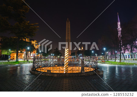 The Serpent Column in Sultanahmet Square, Istanbul, illuminated at night with the spire of the Sultan Ahmed Mosque lit in pink in the background. The Serpent Column in Sultanahmet Square, Istanbul, illuminated at night with the spire of the Sultan Ahmed Mosque lit in pink in the background. 128553232