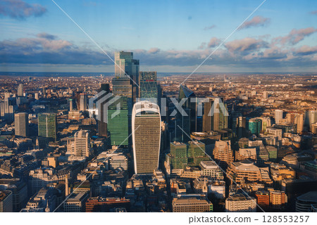 The London skyline features the Walkie Talkie and Cheesegrater skyscrapers, bathed in warm sunlight with a clear blue sky and scattered clouds. 128553257