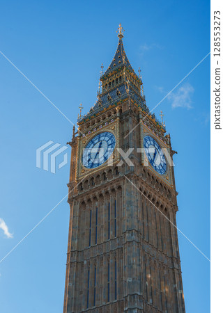 The iconic Elizabeth Tower, known as Big Ben, stands tall in London. Sunlight highlights its Gothic Revival architecture and large clock faces. The iconic Elizabeth Tower, known as Big Ben, stands tall in London. Sunlight highlights its Gothic Revival architecture and large clock faces. 128553273