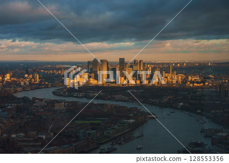 Aerial view of Canary Wharf in London during Christmas, featuring modern skyscrapers like One Canada Square, the River Thames, and dramatic clouds. 128553356