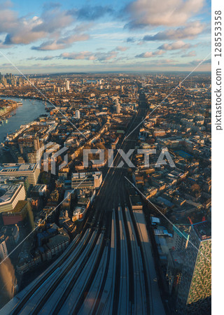 Aerial perspective of London featuring the River Thames, railway tracks to London Bridge Station, and the Shard's shadow under a golden sky. Aerial perspective of London featuring the River Thames, railway tracks to London Bridge Station, and the Shard's shadow under a golden sky. 128553358