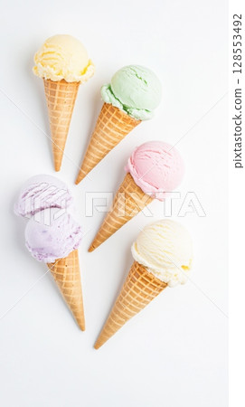 Top view of five mini pastel ice cream cones in a diagonal row, each scoop in a different flavor. Bright, creamy textures perfect for summer ads, packaging, and dessert visuals. 128553492