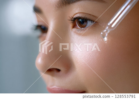 Young woman receiving facial serum under soft light, perfect for skincare branding and cosmetics. Young woman receiving facial serum under soft light, perfect for skincare branding and cosmetics. 128553791