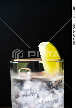 [雞尾酒配料] 在黑色背景下，將一杯美味的金湯力倒入加冰的玻璃杯中 [飲料配料] 128553845