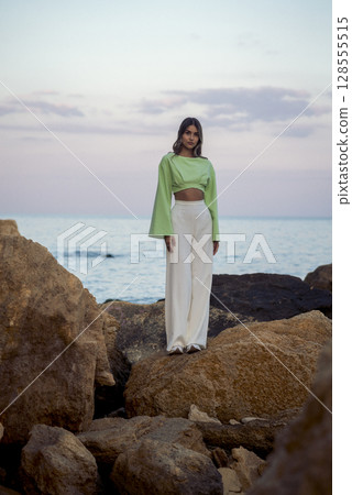 a slender young girl in white trousers stands on the seashore a slender young girl in white trousers stands on the seashore 128555515
