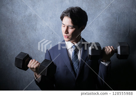 A man in a suit doing muscle training with dumbbells A man in a suit doing muscle training with dumbbells 128555988