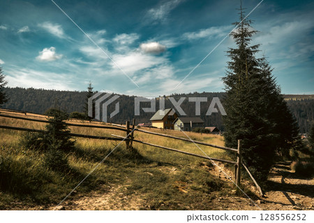 In this calm countryside setting, a simple wooden fence leads toward a home nestled on a hill. 128556252