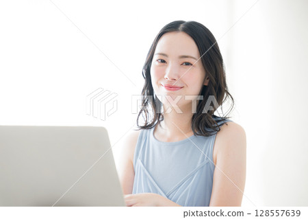 A cute woman in front of a computer looking at the camera, wearing a spring/summer sleeveless white dress and a light blue one-piece 128557639