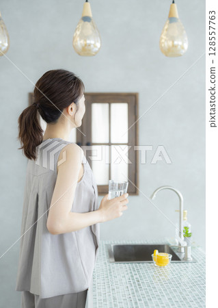 Middle-aged woman drinking water in the kitchen Middle-aged woman drinking water in the kitchen 128557763