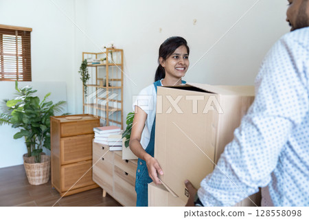Happy Couple Moving into New Home with Cardboard Boxes and Smiling Faces Happy Couple Moving into New Home with Cardboard Boxes and Smiling Faces 128558098