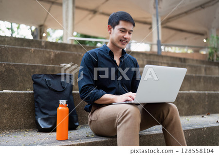 Young Professional Working on Laptop Outdoors in Casual Setting Young Professional Working on Laptop Outdoors in Casual Setting 128558104