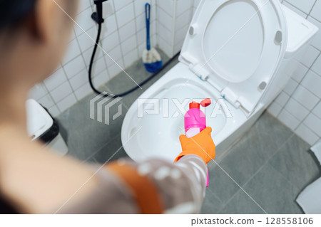Woman Cleaning Toilet with Cleaning Product in Modern Bathroom, Wearing Orange Gloves, Close-Up View 128558106