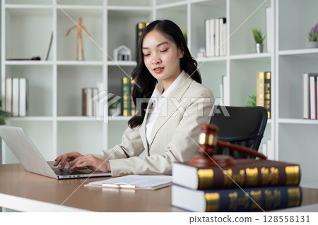 Professional Businesswoman Working on Laptop in Modern Office with Bookshelves and Legal Books Professional Businesswoman Working on Laptop in Modern Office with Bookshelves and Legal Books 128558131