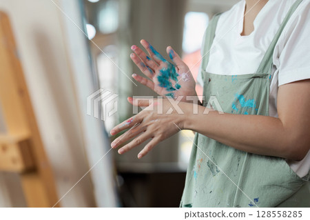 Artist with Paint-Splattered Hands in Apron Creating Art in Studio Artist with Paint-Splattered Hands in Apron Creating Art in Studio 128558285
