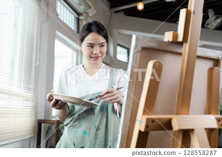 Young Female Artist Painting on Canvas in a Bright Studio with Natural Light and Modern Interior Design Young Female Artist Painting on Canvas in a Bright Studio with Natural Light and Modern Interior Design 128558287