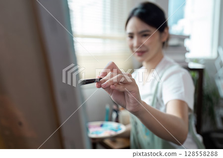 Woman Painting on Canvas in Bright Studio with Natural Light and Artistic Ambiance Woman Painting on Canvas in Bright Studio with Natural Light and Artistic Ambiance 128558288