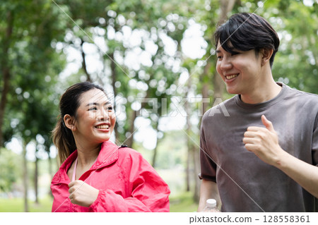 Happy Young Couple Jogging Together in a Park on a Bright Day, Enjoying Outdoor Exercise and Healthy Lifestyle Happy Young Couple Jogging Together in a Park on a Bright Day, Enjoying Outdoor Exercise and Healthy Lifestyle 128558361