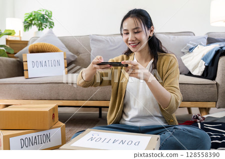 Young Woman Taking Photos of Donation Boxes in Living Room for Charity and Community Support 128558390