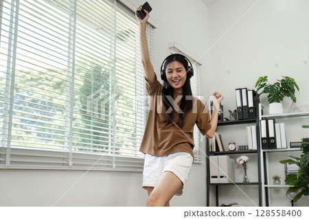 Young Woman Enjoying Music with Headphones and Smartphone in Modern Home Office Environment 128558400