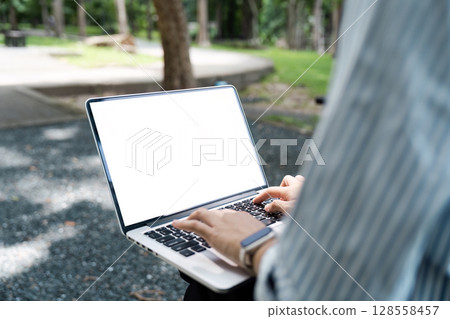 Person Using Laptop with Blank Screen Outdoors in a Park Setting Person Using Laptop with Blank Screen Outdoors in a Park Setting 128558457