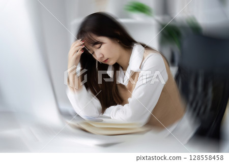 Young Woman Feeling Sick at Work, Experiencing Headache and Fatigue in Office Environment Young Woman Feeling Sick at Work, Experiencing Headache and Fatigue in Office Environment 128558458