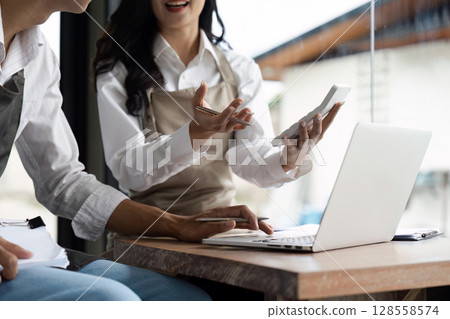 Young Entrepreneurs Collaborating on Business Strategy in Modern Cafe Setting with Laptop and Smartphone Young Entrepreneurs Collaborating on Business Strategy in Modern Cafe Setting with Laptop and Smartphone 128558574