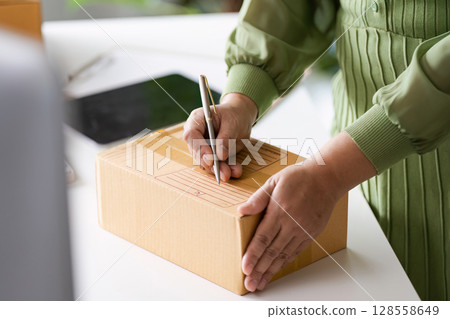 Small Business Owner Preparing a Package for Shipping in a Modern Home Office Environment Small Business Owner Preparing a Package for Shipping in a Modern Home Office Environment 128558649
