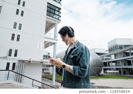 Young Man Enjoying Music on Smartphone While Traveling in Modern Urban Cityscape 128558654