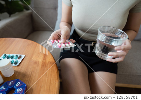 Woman Holding Medication and Glass of Water, Emphasizing Healthcare and Wellness in a Home Setting 128558701