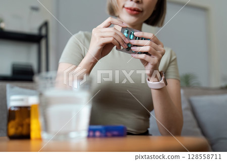 Woman Organizing Medication at Home with Pill Organizer and Glass of Water on Table 128558711