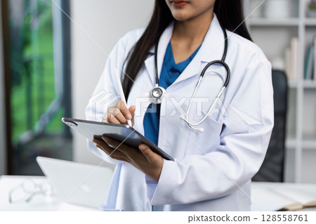 Female Doctor Using Digital Tablet in Modern Medical Office with Stethoscope Around Neck Female Doctor Using Digital Tablet in Modern Medical Office with Stethoscope Around Neck 128558761