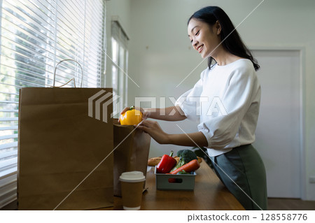 Woman Unpacking Groceries in Modern Kitchen with Natural Light and Fresh Vegetables 128558776