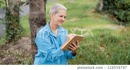 Senior Woman Reading a Book Outdoors in a Park on a Sunny Day Senior Woman Reading a Book Outdoors in a Park on a Sunny Day 128558787