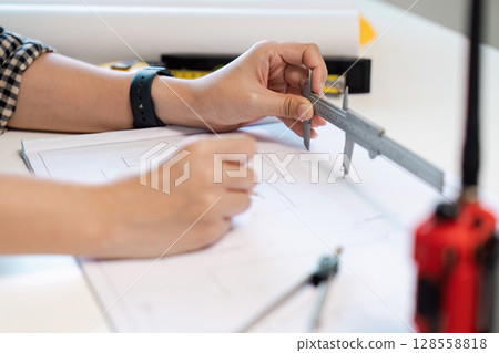 Engineer Measuring Blueprint with Caliper in Modern Office Setting for Precision and Accuracy in Design 128558818