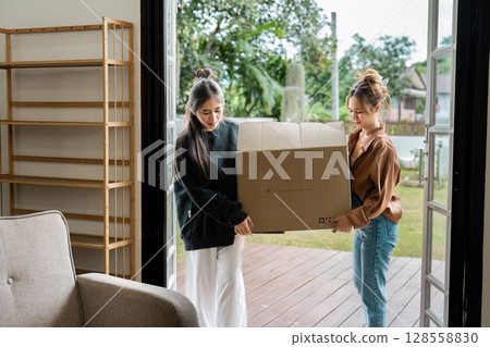 Young Women Moving House, Carrying Cardboard Box into New Home, Relocation and Moving Day Concept Young Women Moving House, Carrying Cardboard Box into New Home, Relocation and Moving Day Concept 128558830