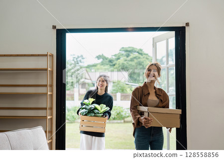 Happy Family Moving into New Home with Boxes and Plants, Excited Women Entering Modern House, Fresh Start and New Beginnings 128558856