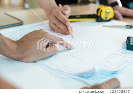Engineer Working on Blueprint with Pencil and Measuring Tape in Modern Office Engineer Working on Blueprint with Pencil and Measuring Tape in Modern Office 128558897