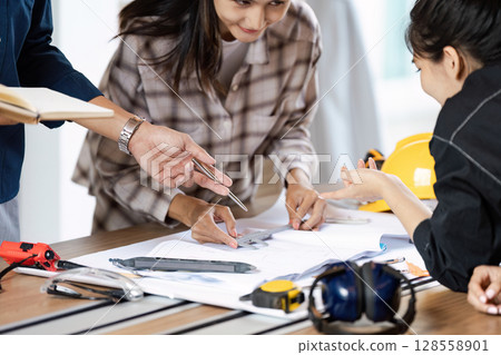 Team of Engineers Collaborating on Project Plans at Modern Workspace with Tools and Safety Gear Team of Engineers Collaborating on Project Plans at Modern Workspace with Tools and Safety Gear 128558901