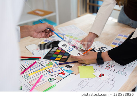 Creative Team Collaborating on UX UI Design with Colorful Prototypes and Wireframes on a Wooden Desk 128558926