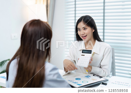 Professional Business Meeting with Two Women Discussing Financial Reports and Using a Calculator in a Modern Office Professional Business Meeting with Two Women Discussing Financial Reports and Using a Calculator in a Modern Office 128558938
