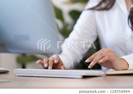 Professional Businesswoman Typing on Keyboard in Modern Office Environment with Green Plant Background 128558944
