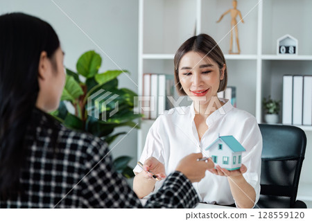 Real Estate Agent Handing Over House Model to Client in Modern Office Setting 128559120