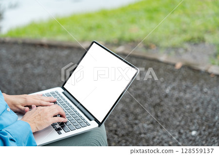 Person Typing on Laptop with Blank Screen Outdoors on a Gravel Path with Green Grass Background Person Typing on Laptop with Blank Screen Outdoors on a Gravel Path with Green Grass Background 128559137